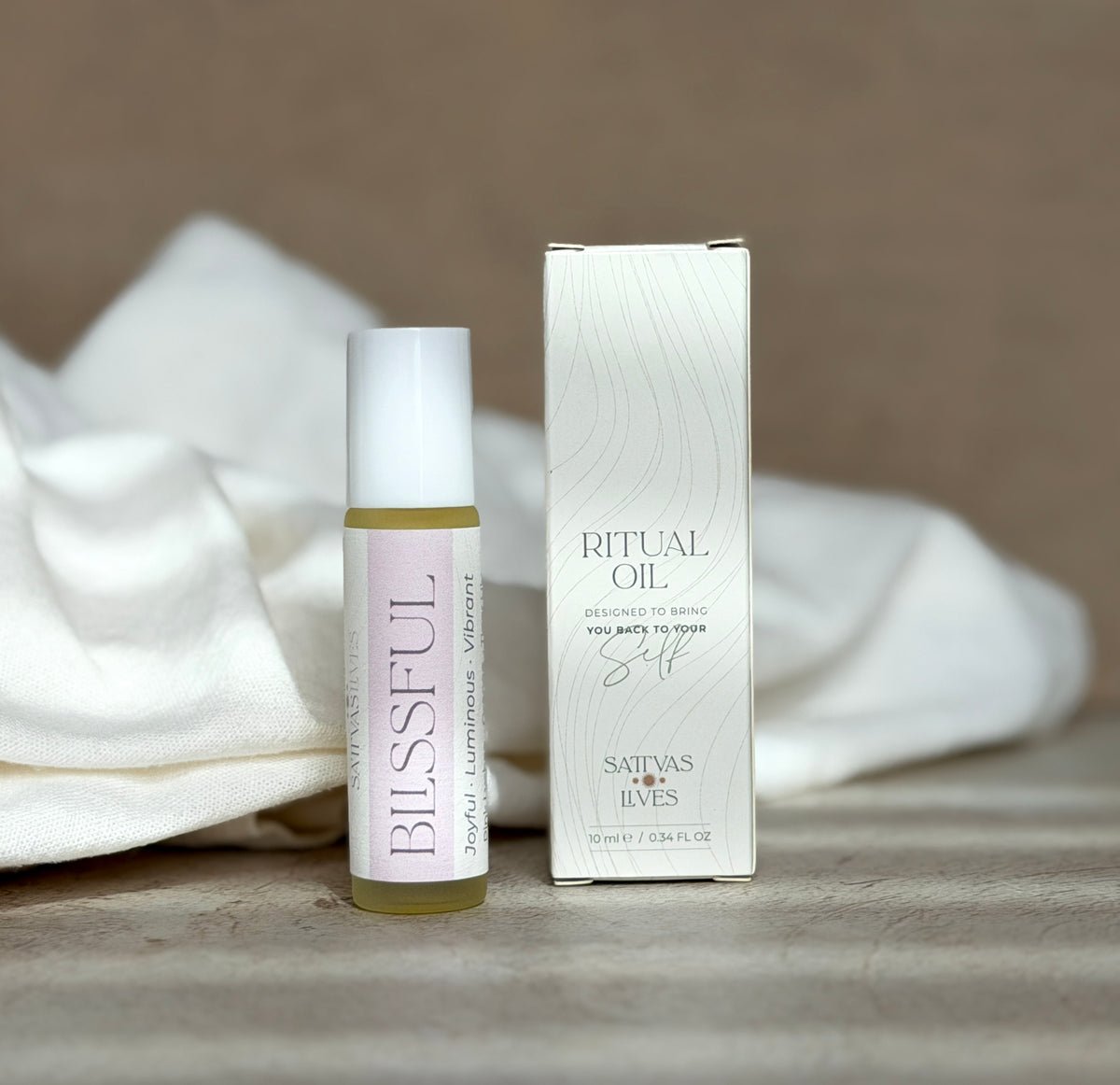 A small glass roll-on bottle labeled BLISSFUL next to its white box, set on a neutral surface with soft white fabric in the background.