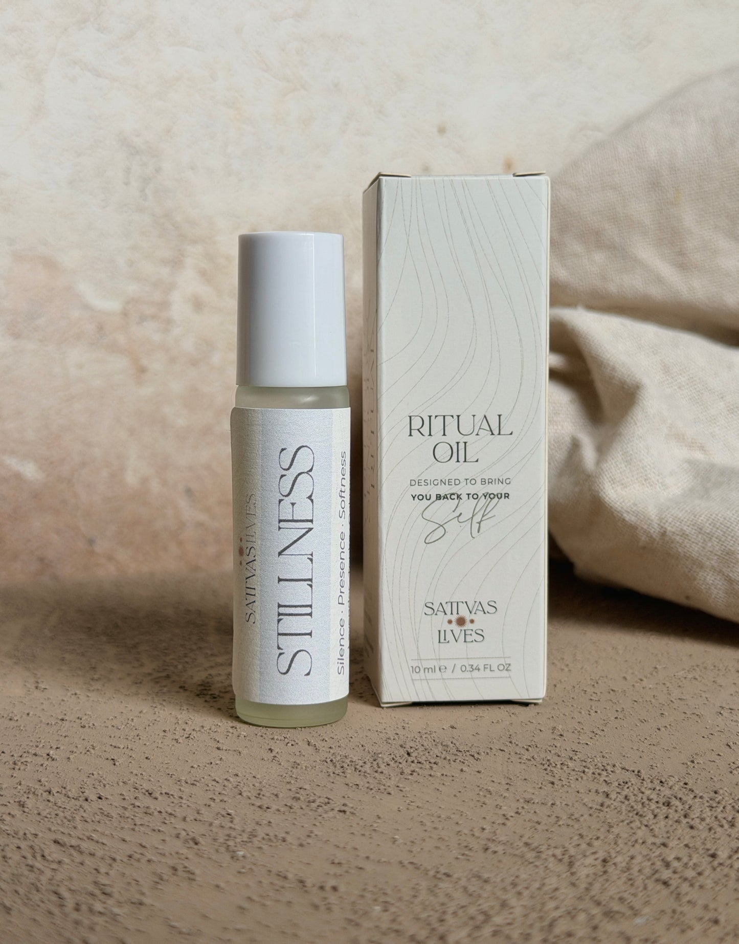 A small glass bottle of Satva's Luxe Ritual Oil with a white cap stands next to its white textured packaging box on a neutral beige surface.