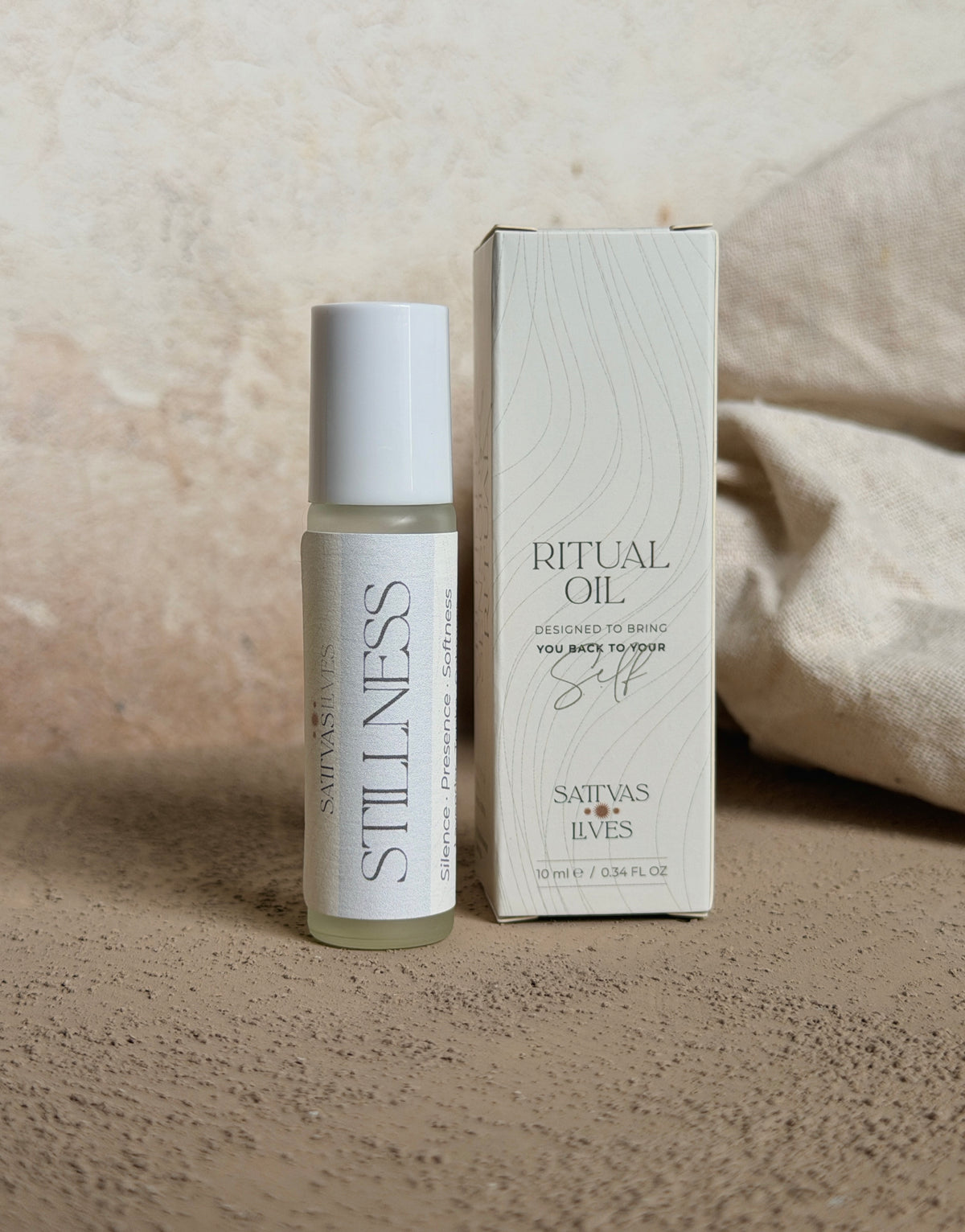 A small glass bottle of Satva's Luxe Ritual Oil with a white cap stands next to its white textured packaging box on a neutral beige surface.